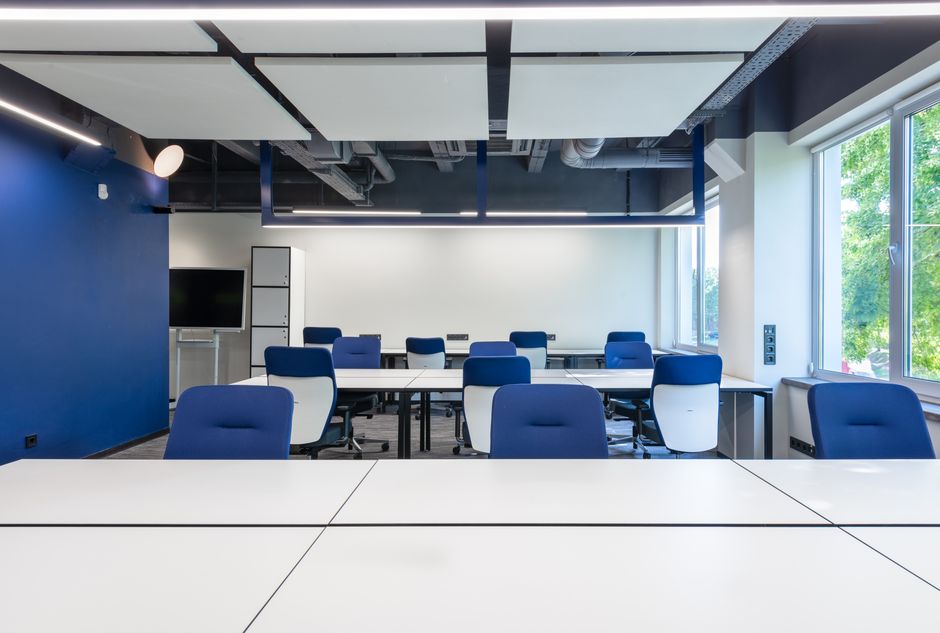 Various white desks with blue chairs placed in modern spacious workspace